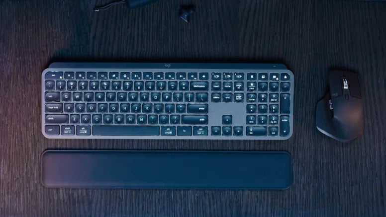 Schwarze Logitech Wireless Tastatur mit Handballenauflage und passender ergonomischer Maus auf dunklem Holzschreibtisch.