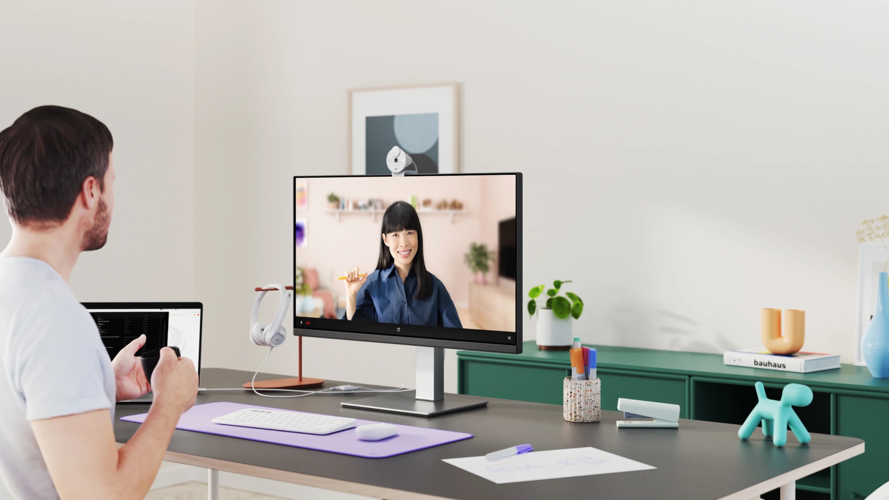 Mann an einem modernen Schreibtisch mit Monitor, Webcam und Laptop im Homeoffice.