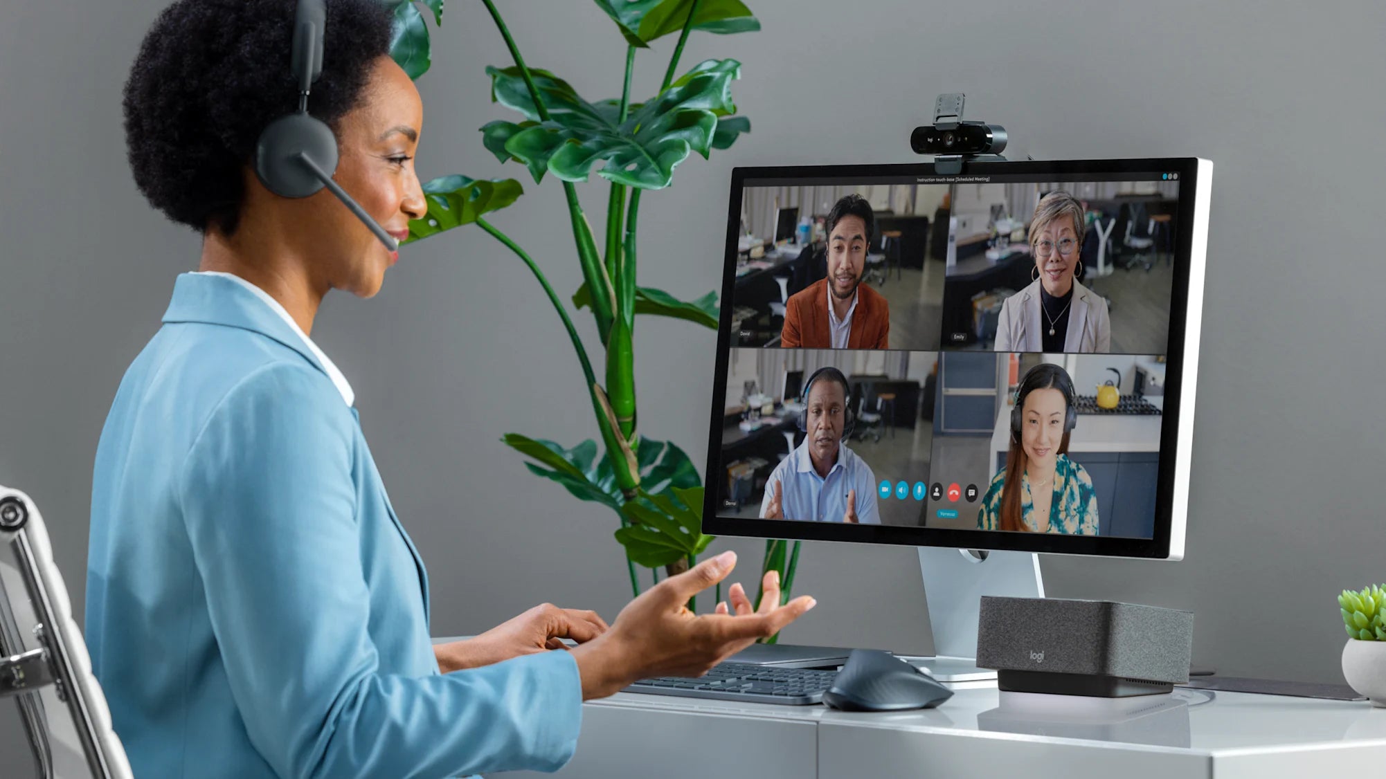 Frau führt in modernem Home-Office eine Videokonferenz mit Business-Headset über Monitor und HD-Webcam.