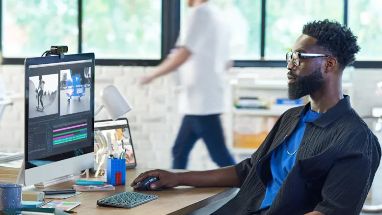 Ein Content Creator arbeitet an einem modernen Arbeitsplatz mit Monitor, Webcam, kompakter Tastatur und ergonomischer Maus.