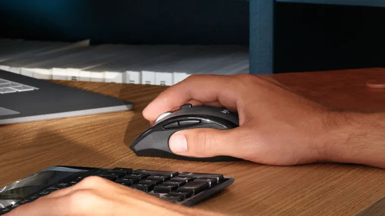 Hand bedient eine ergonomische Computer-Maus auf einem Holztisch neben einer Tastatur und einem Laptop