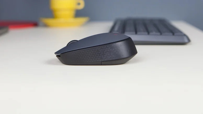 Schwarze Wireless-Computermaus in Seitenansicht auf hellem Schreibtisch mit Tastatur und gelber Tasse im Hintergrund.