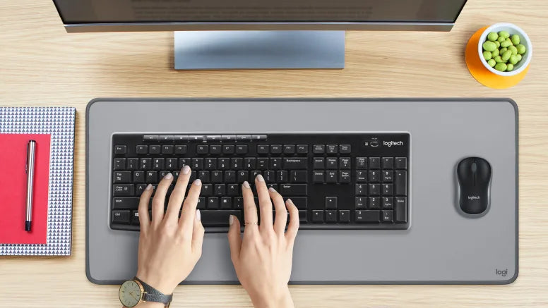 Hände tippen auf einer schwarzen Logitech-Tastatur auf einer Schreibtischunterlage neben einer Computermaus.