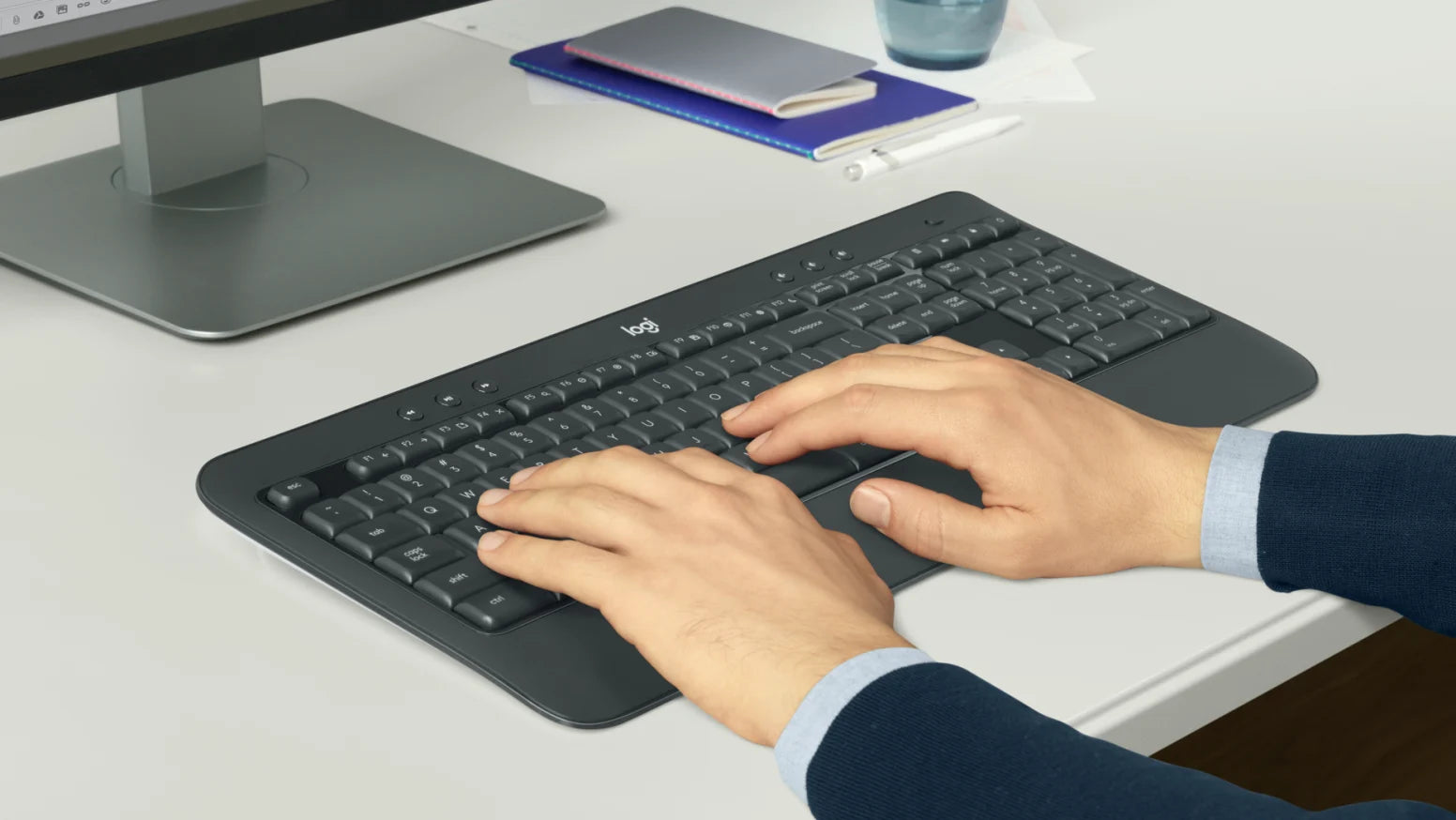 Hände tippen auf einer ergonomischen Logitech-Tastatur an einem hellen Schreibtisch