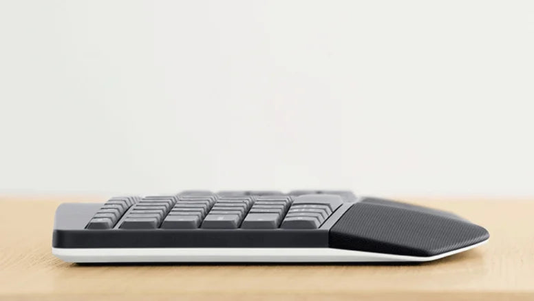 Seitenansicht einer ergonomischen Tastatur mit integrierter Handballenauflage auf einem Holztisch