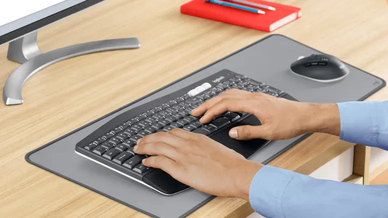 Hände tippen auf ergonomischer kabelloser Logitech Tastatur auf Schreibtisch mit Maus und Mauspad.