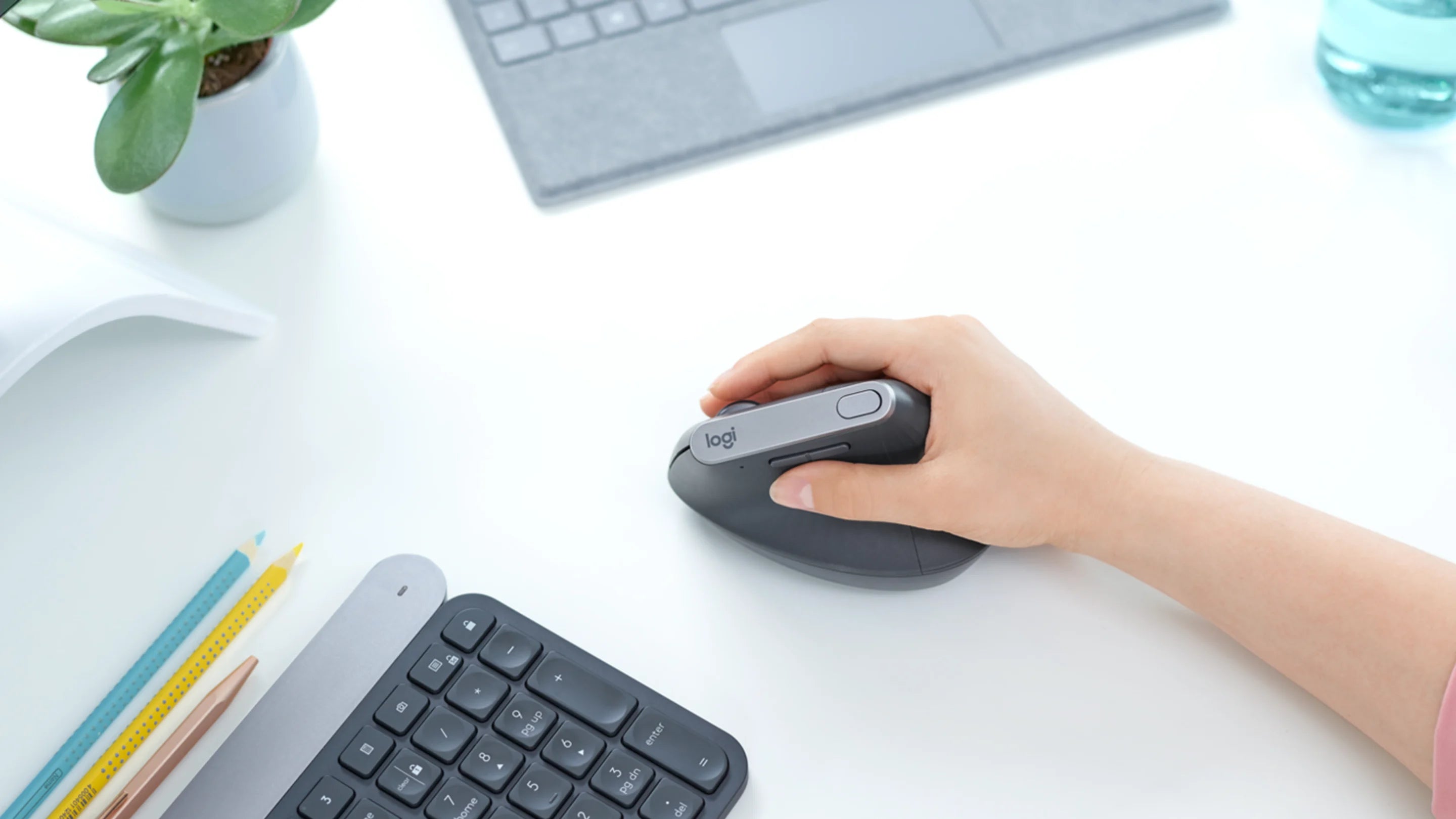 Hand bedient eine ergonomische Logitech MX Vertical Maus auf einem hellen Schreibtisch mit Tastatur.