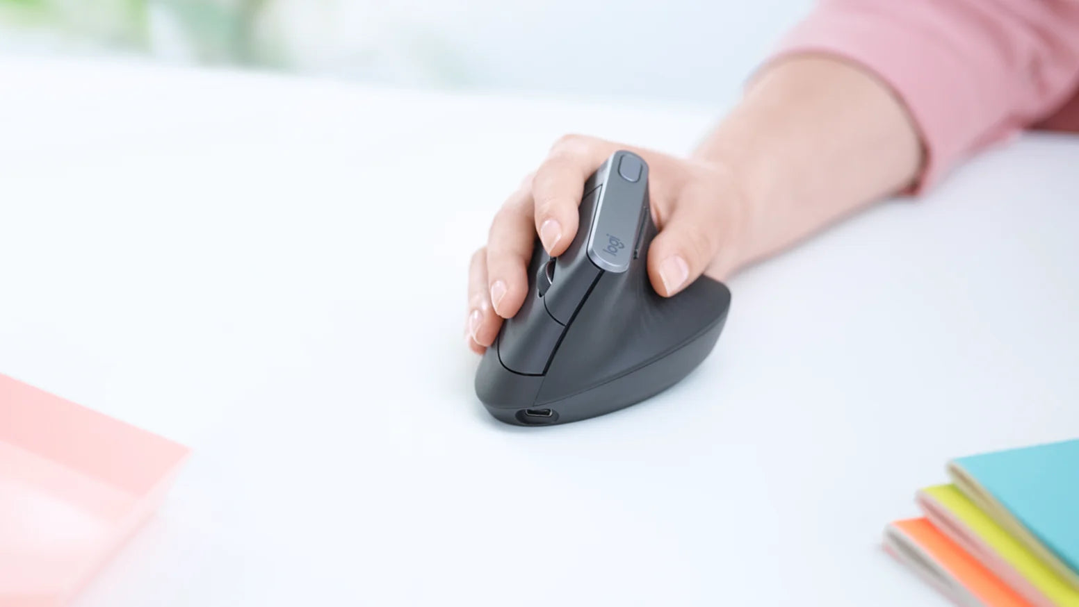 Hand bedient eine ergonomische Logitech Vertikal-Maus auf einem hellen Schreibtisch.