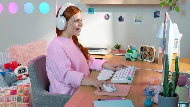 Frau mit Headset und rosa Pullover bedient weiße Gaming-Tastatur und Maus am aufgeräumten Schreibtisch